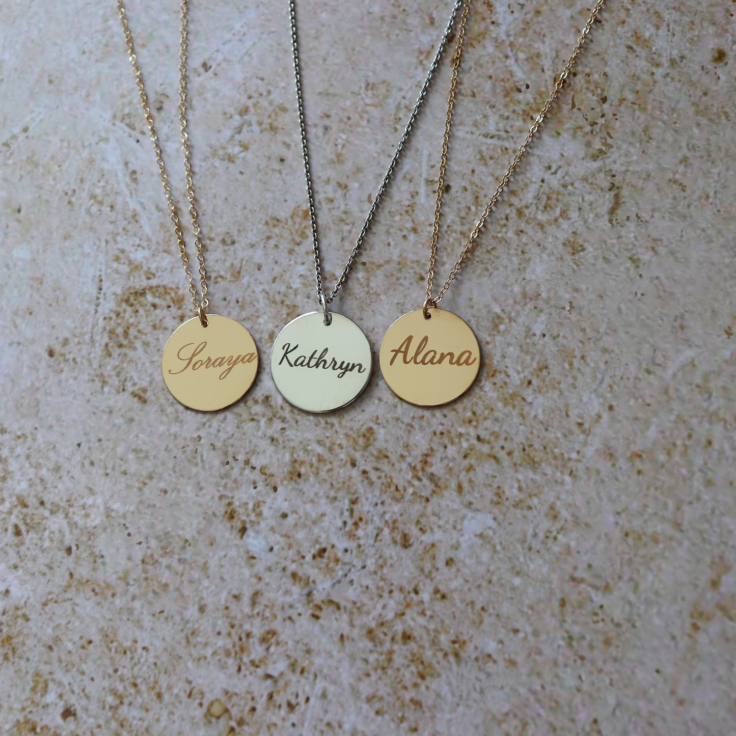 Three gold necklaces with engraved names on a textured surface