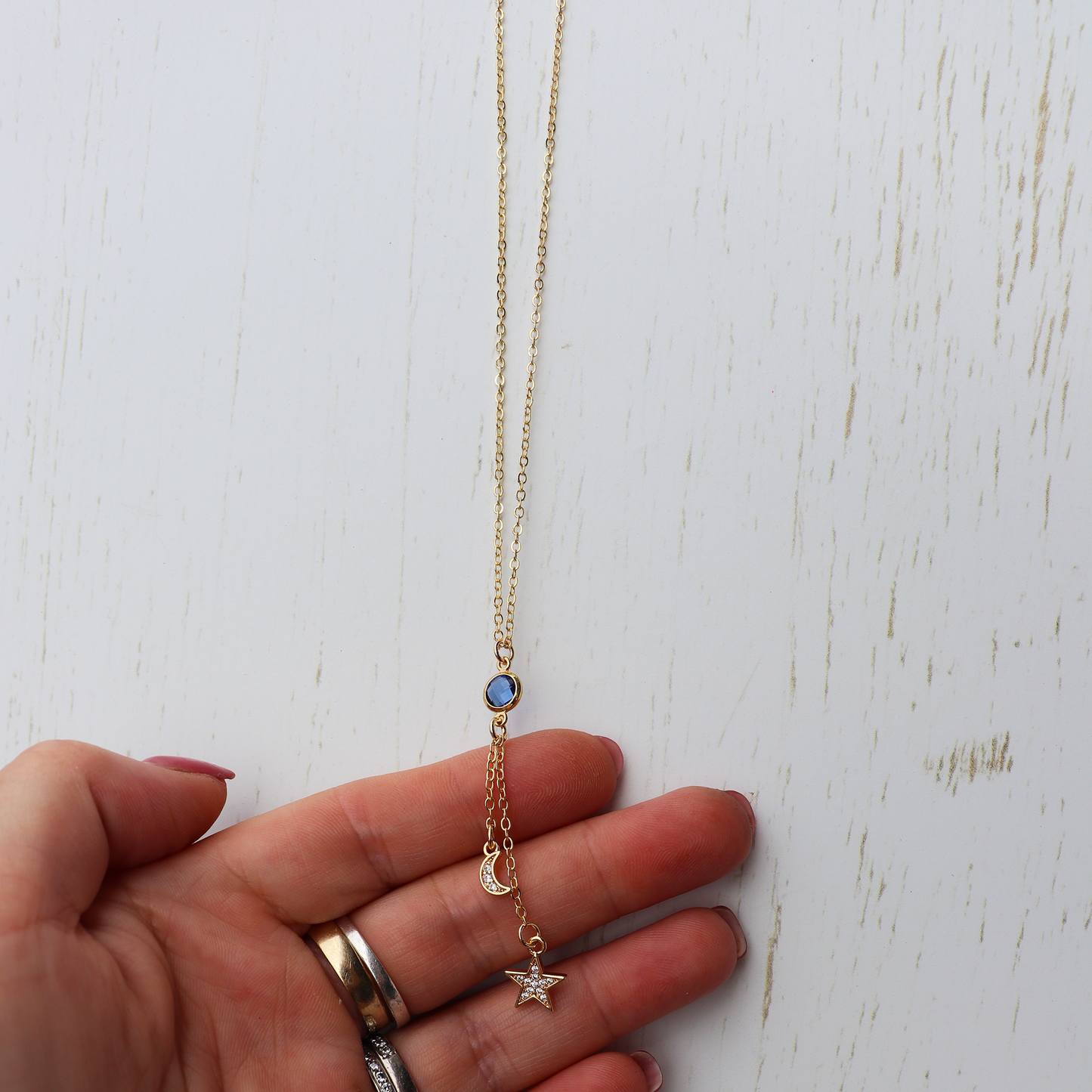 Hand holding a gold necklace with star and blue gemstone pendant on a white surface