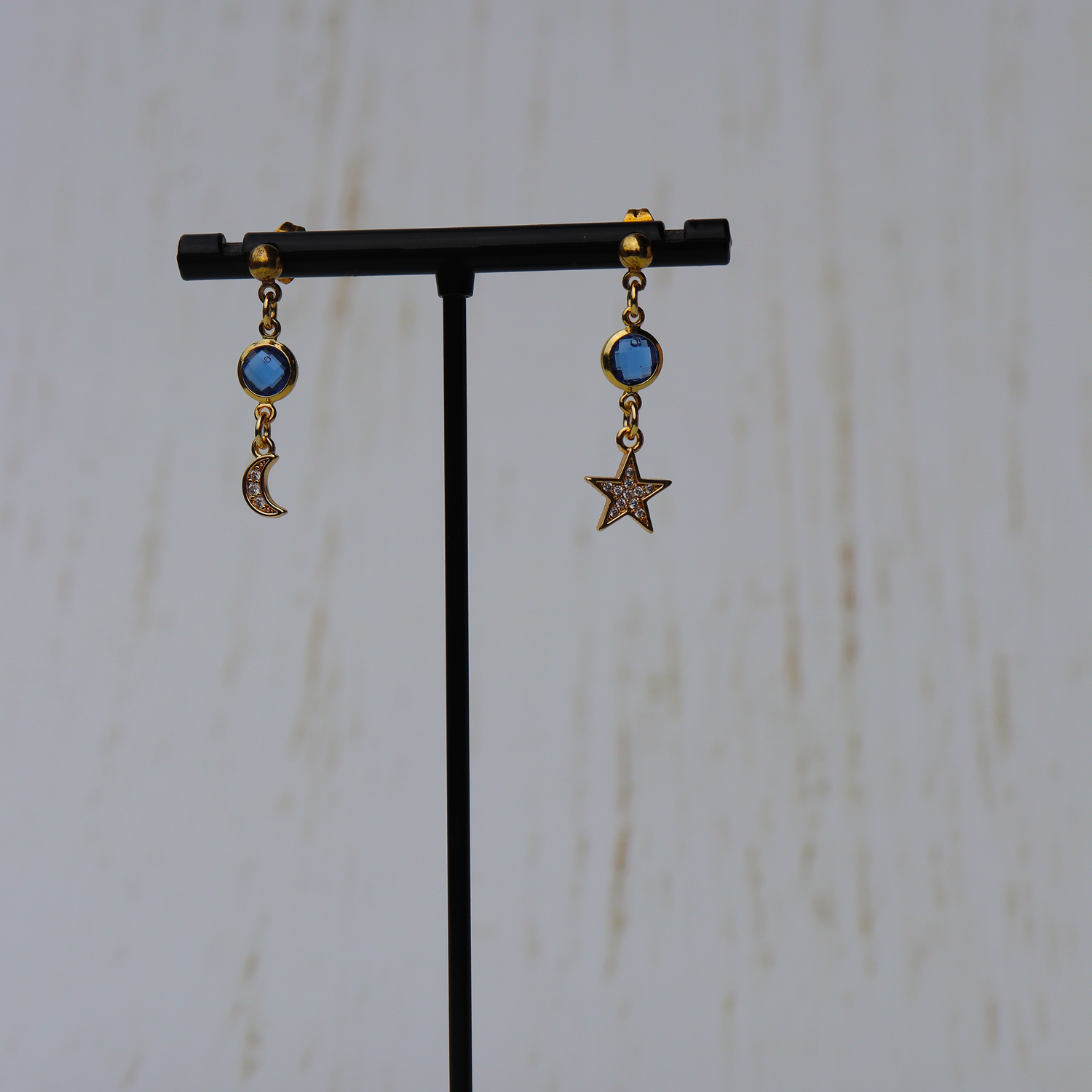 Pair of earrings with star and moon designs on a black stand against a white background
