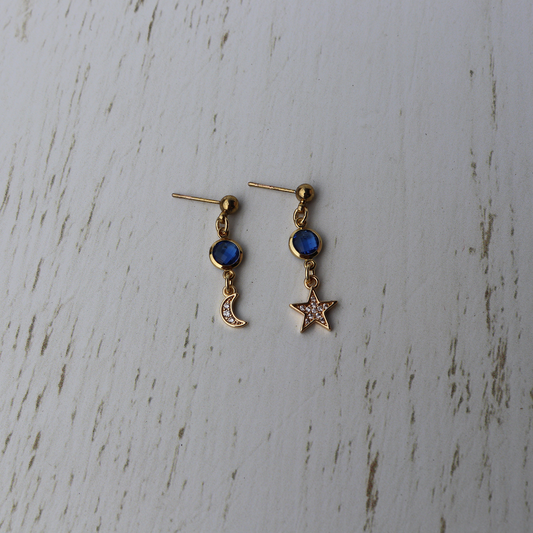 Pair of gold earrings with blue gemstones on a textured white surface